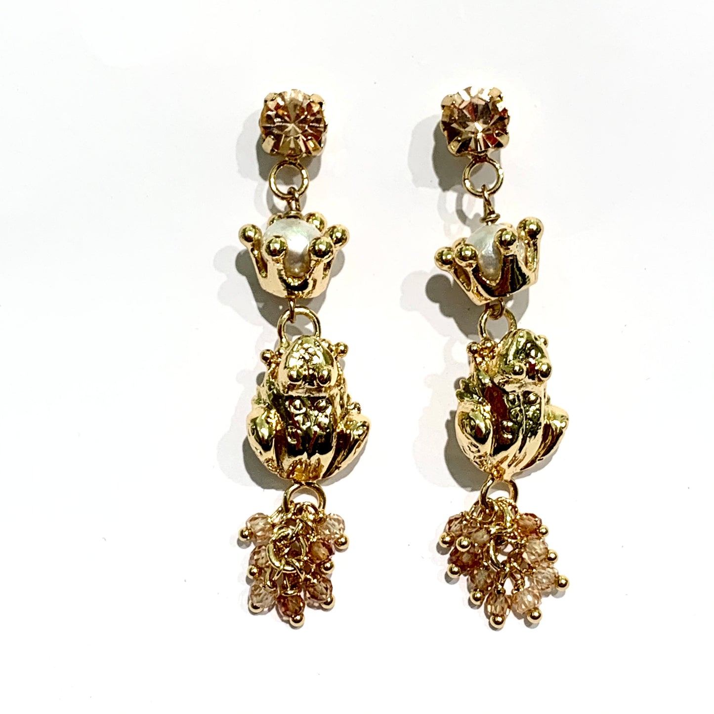 Orecchini in bronzo placcato in oro 24kt composti da uno zircone colore rosa pesca a cui è attaccata una corona impreziosita da una perla coltivata all'interno, con ranocchie pendenti e perline rosa pesca. Lunghezza totale 6 cm. Larghezza ranocchia 0,8 cm. Chiusura con farfalline. Spedizione gratuita con confezione.