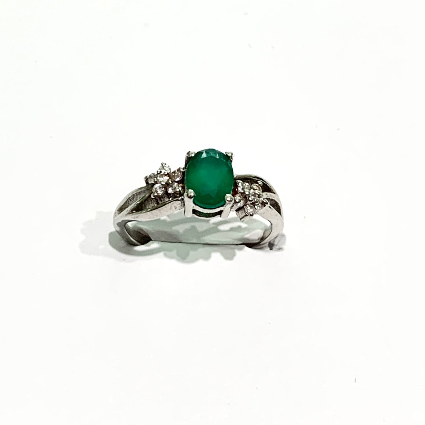 Anello in argento con pietra in radice di smeraldo e piccoli zirconi bianchi che formano due fiorellini laterali. Dimensioni pietra 0,7x0,4 cm. Misura 13.