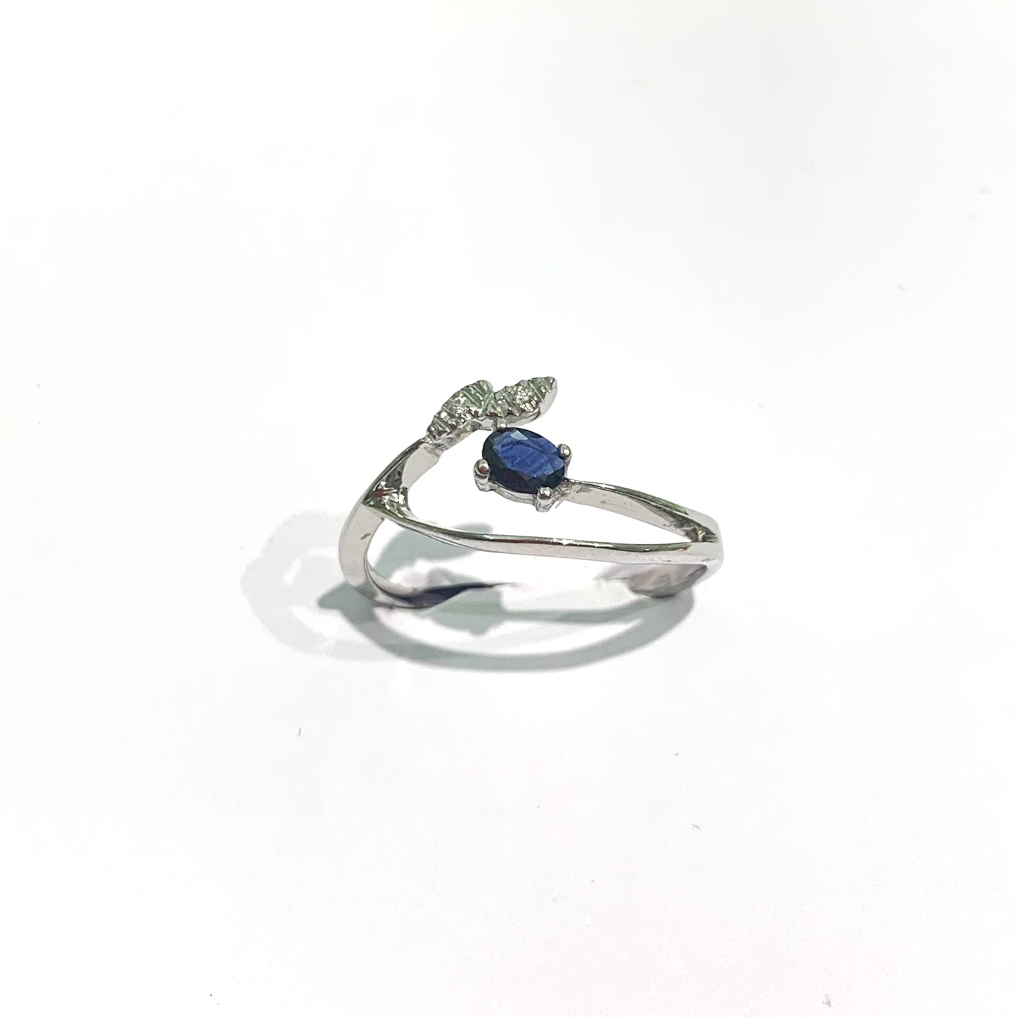 Anello in oro bianco 18kt con fogliolina ricoperta di diamanti e zaffiro centrale. Caratura diamanti 0,01. Dimensione 0,4x0,2 cm. Misura 16.