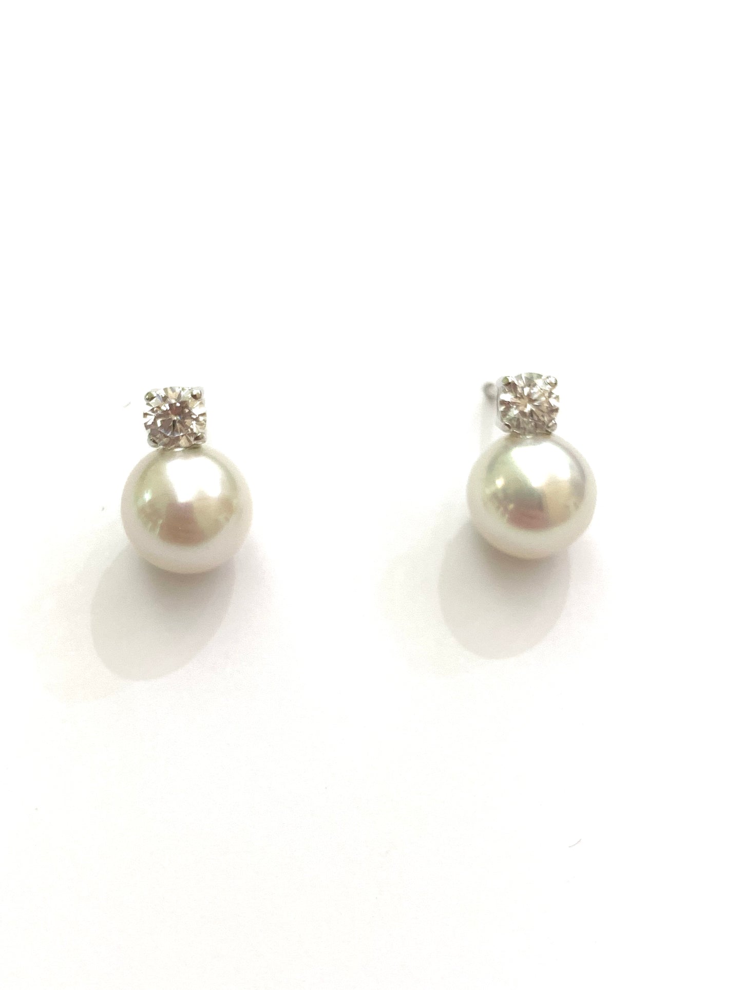 Orecchini in oro bianco 18kt con perle coltivate impreziosite da uno zircone. Dimensione perla 0,7 cm. Dimensione zircone 0,3 cm. Chiusura con farfalline.