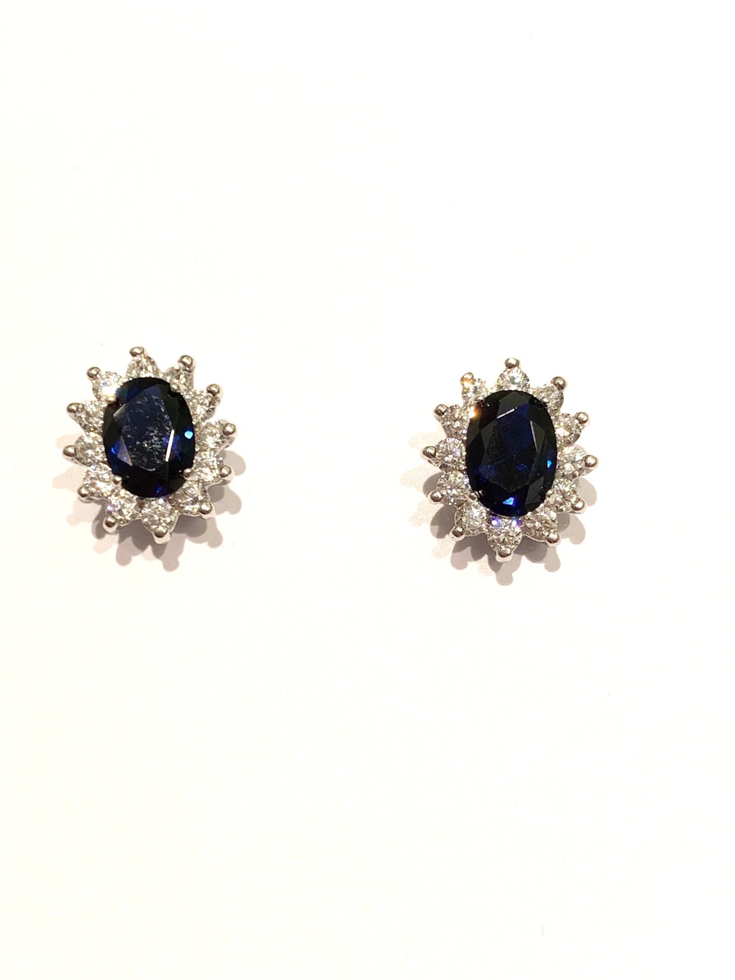 Orecchini in oro bianco 9kt con zircone ovale colore zaffiro impreziosito da piccoli zirconi bianchi. Dimensione totale 0,6x1 cm. Chiusura con farfalline.