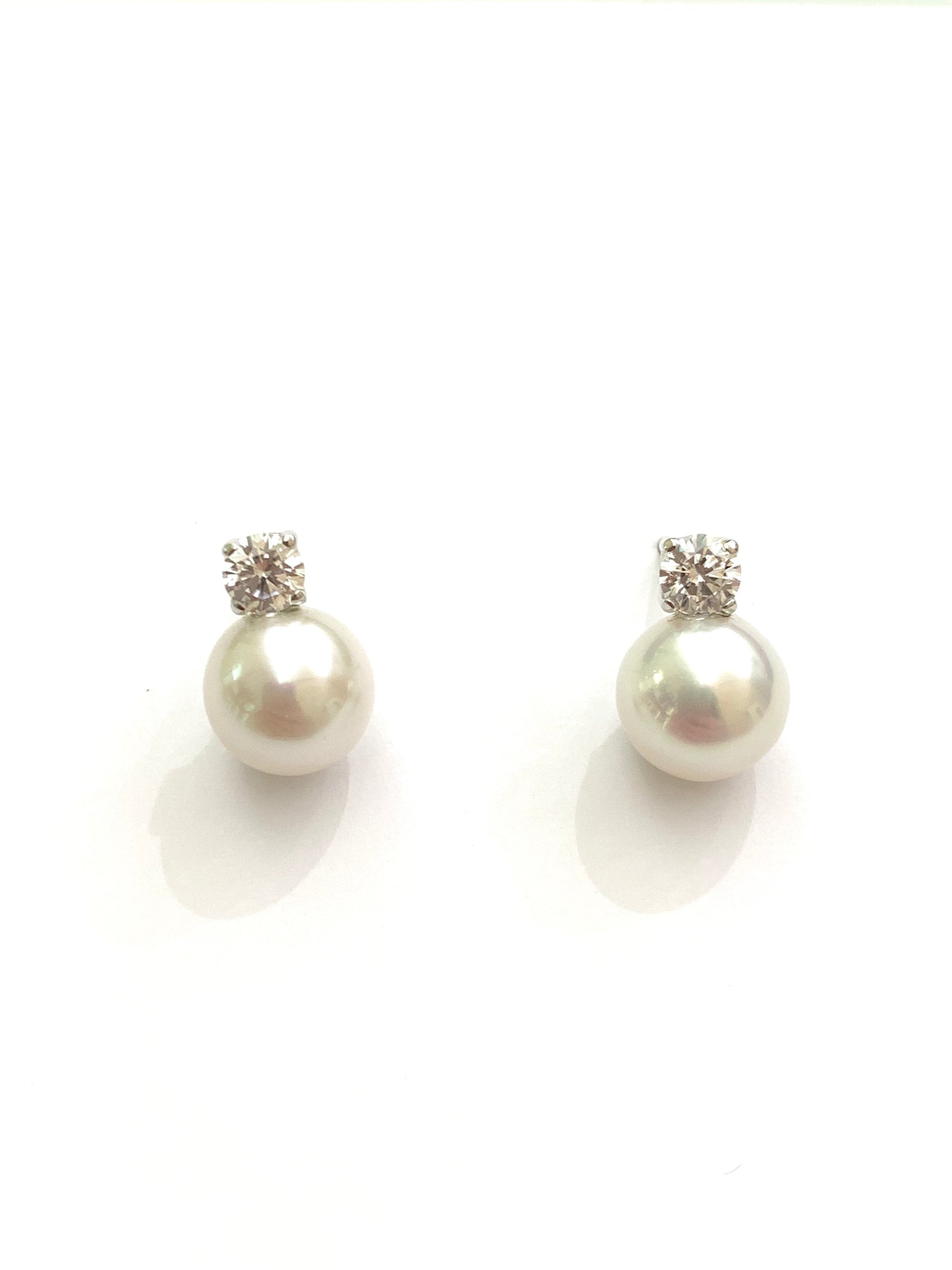 Orecchini in oro bianco 18kt con perle coltivate impreziosite da uno zircone. Dimensione perla 0,7 cm. Dimensione zircone 0,3 cm. Chiusura con farfalline.