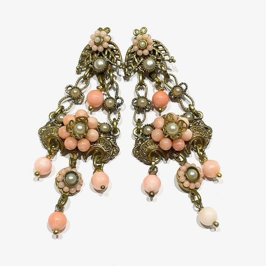 Orecchini pendenti in bijoux bagnati in oro giallo con perline color corallo rosa.

Lunghezza totale 6,5 cm.

Larghezza nella parte più ampia 3 cm.

Chiusura con farfalline.