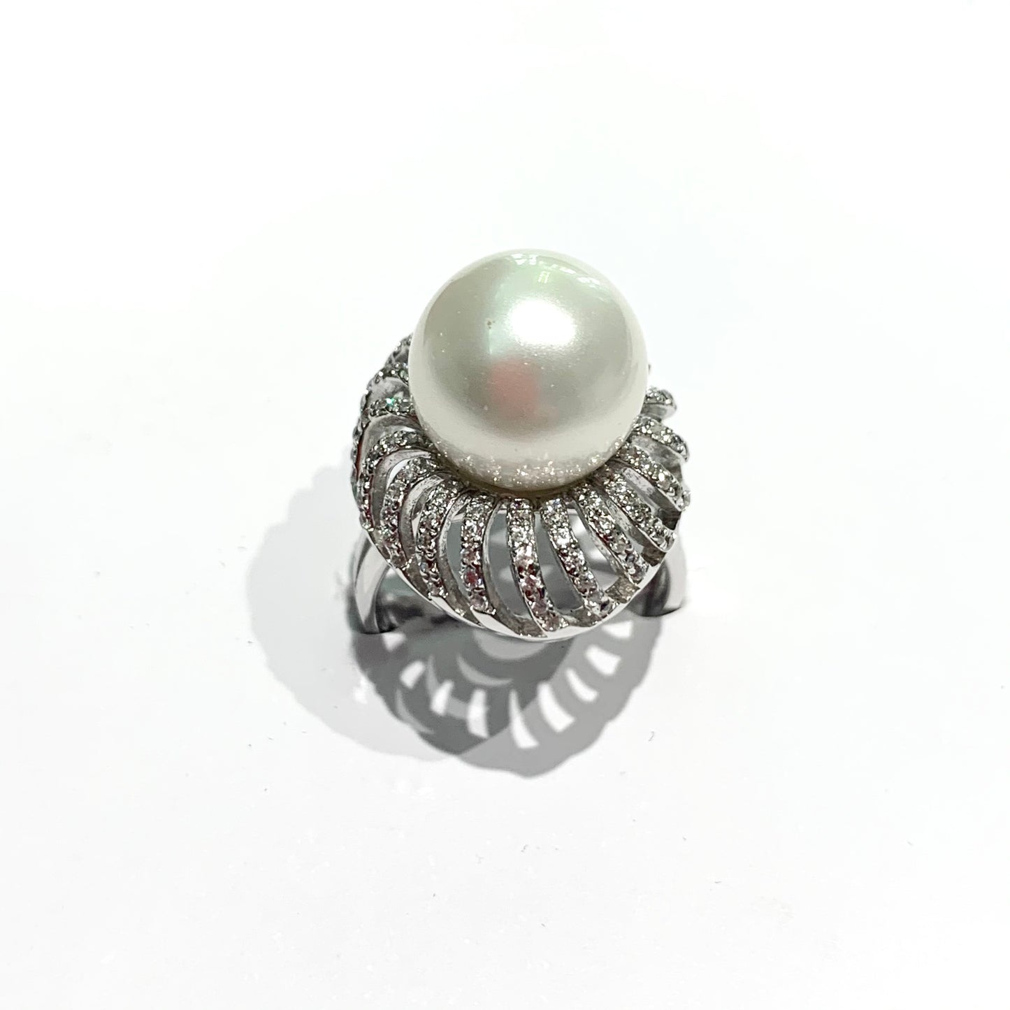 Anello in argento con perla coltivata centrale circondata da zirconi.  Dimensioni perla 1 cm.  Dimensione totale 1,7x2,3 cm.  Misura regolabile da 13 a 17.