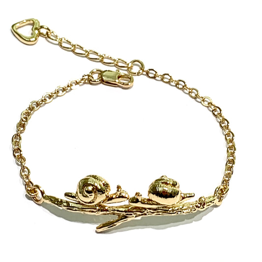 Bracciale in bronzo bagnato nell'oro 24kt trattato con cataforesi per garantirne la brillantezza nel tempo, impreziosito da una coppia di soggetti appoggiata su un rametto. Disponibile con la coppia di uccellini oppure con le lumache. Lunghezza regolabile da 18 cm a 21 cm. Lunghezza rametto 5 cm. Altezza lumachine/uccellini 1 cm. Spedizione gratuita con confezione regalo.