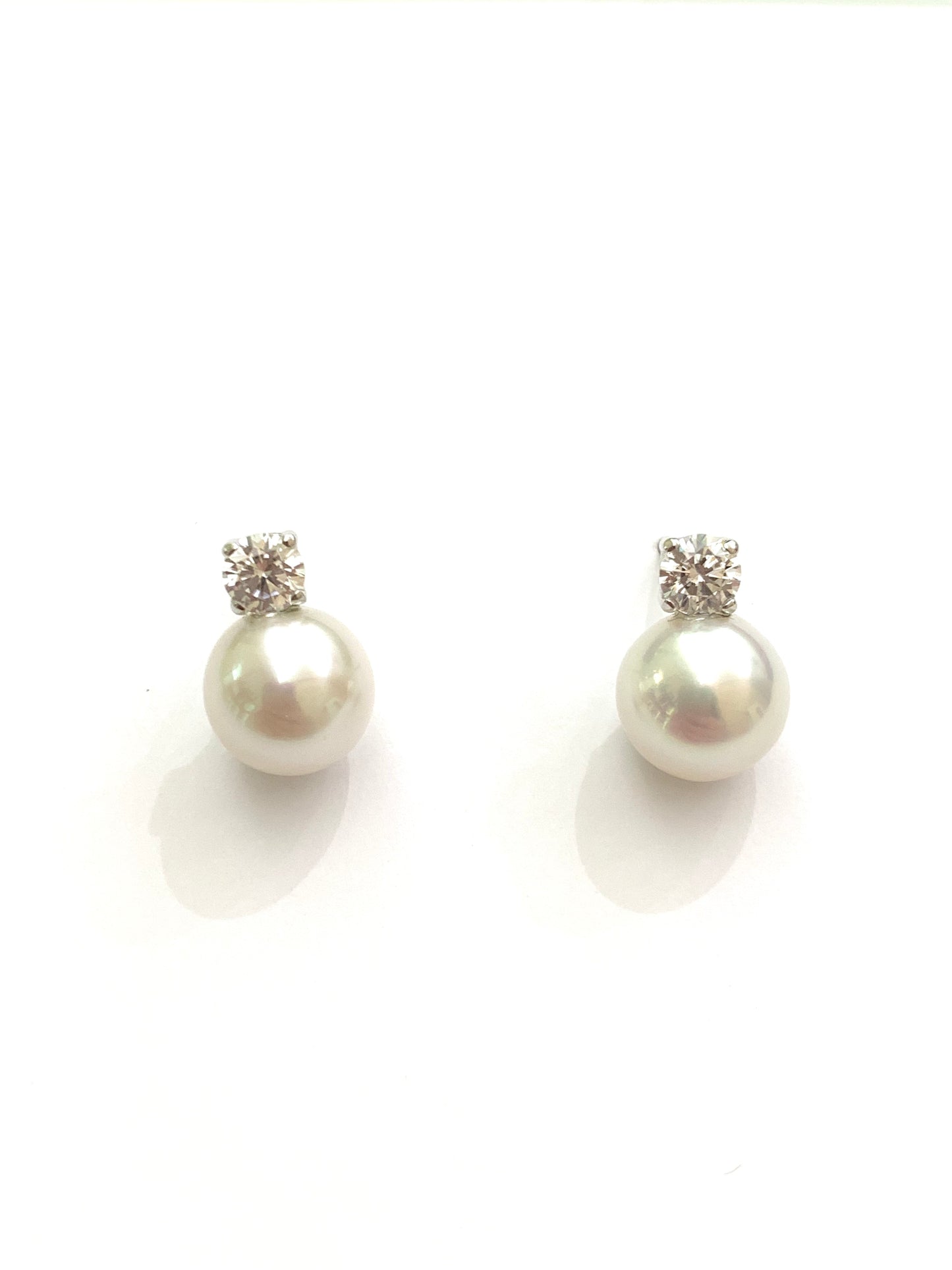 Orecchini in oro bianco 18kt con perle coltivate impreziosite da uno zircone.  Dimensione perla 0,7 cm.  Dimensione zircone 0,3 cm.  Chiusura con farfalline.