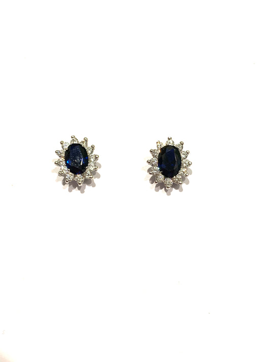 Orecchini in oro bianco 9kt con zircone ovale colore zaffiro impreziosito da piccoli zirconi bianchi. Dimensione totale 0,6x1 cm. Chiusura con farfalline.